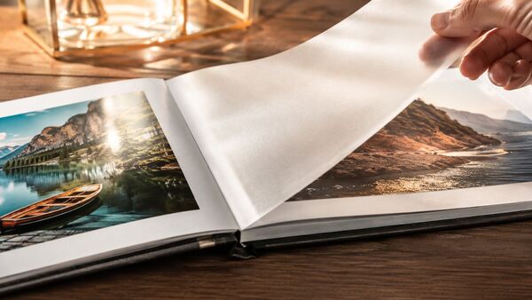Premium-Fotoalbum mit silikonisierten Trennblättern zum Schutz hochwertiger Fotografien Geöffnetes Premium-Fotoalbum mit transparenten silikonisierten Trennblättern zwischen hochglänzenden Fotografien auf edlem Holztisch im warmen Tageslicht – hochwertige Schutzlösung für Fotoabzüge und Erinnerungen.