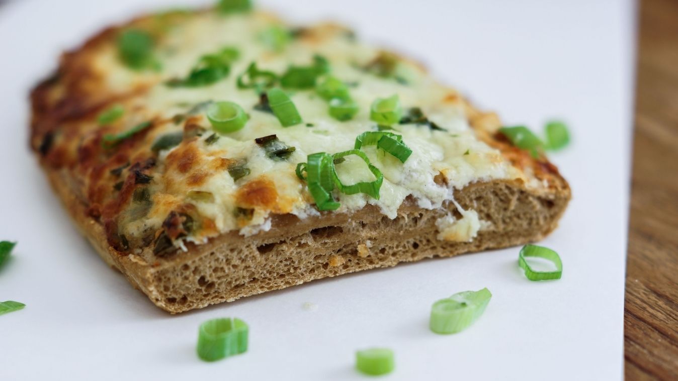 Savory baked snack on Blechrein baking board, topped with cream cheese and green spring onions.